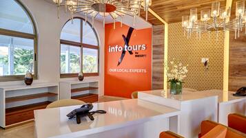 A modern reception area with a large desk, a chandelier, and a wall with a logo.