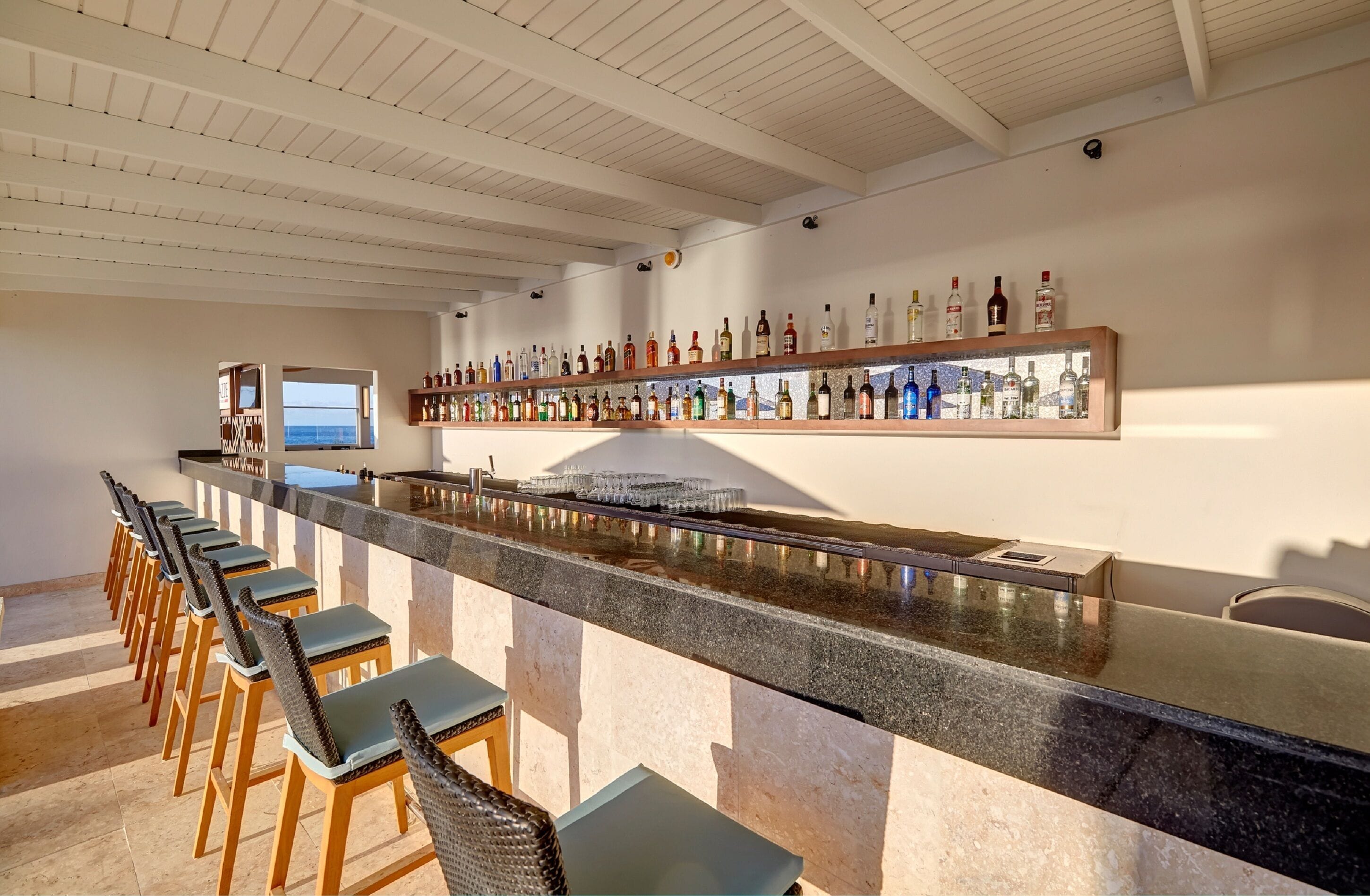 A bar area with a long counter, multiple stools, and a wall of liquor bottles.