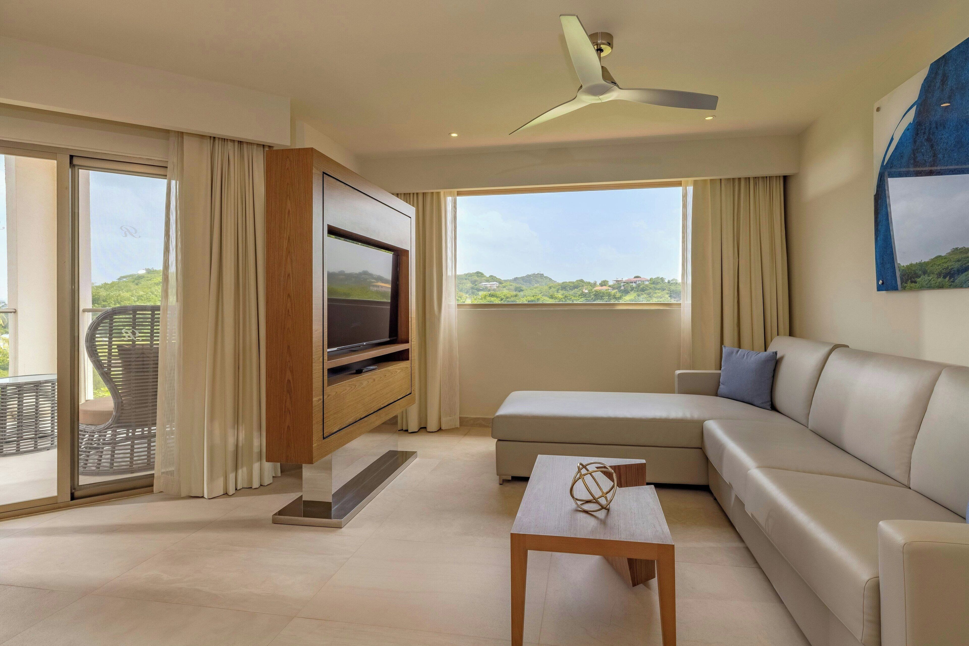 Una sala de estar moderna con un televisor de pantalla plana, un sofá color beige, una mesa de centro de madera y un ventilador de techo.