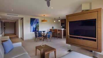 A modern living room with a large flat-screen TV, a ceiling fan, and a dining area with blue chairs.