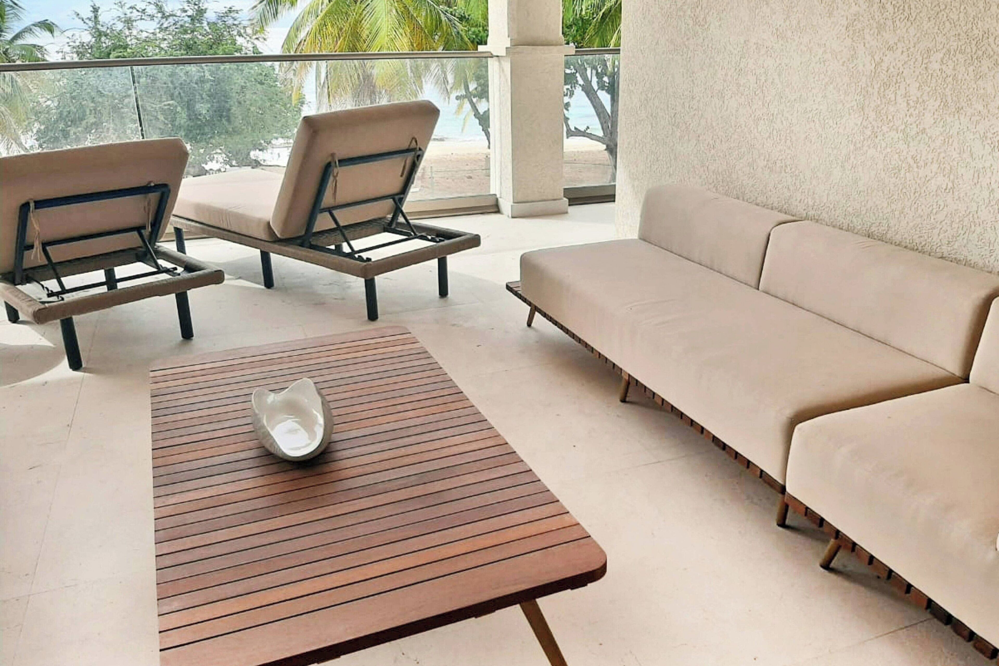 Ein Balkon mit Holztisch, zwei Liegestühlen und einem beigen Sofa.