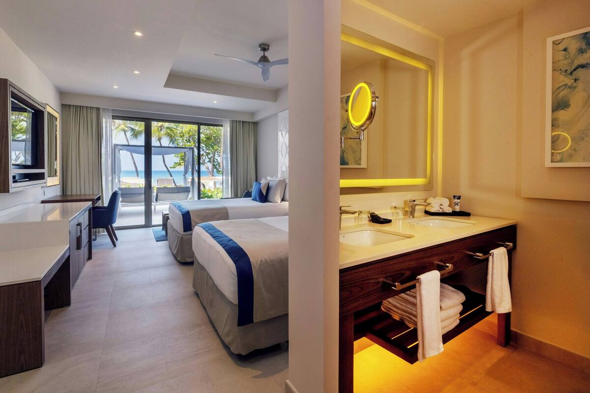 A hotel room with a bed, desk, chair, and a bathroom with a mirror and sink.