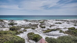 Un paysage côtier avec un sentier sinueux menant à la plage, entouré d’une végétation clairsemée et d’un terrain sablonneux.