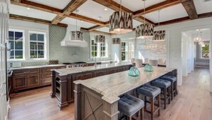 Une cuisine spacieuse dotée d’un grand îlot central, de poutres en bois et de luminaires suspendus.