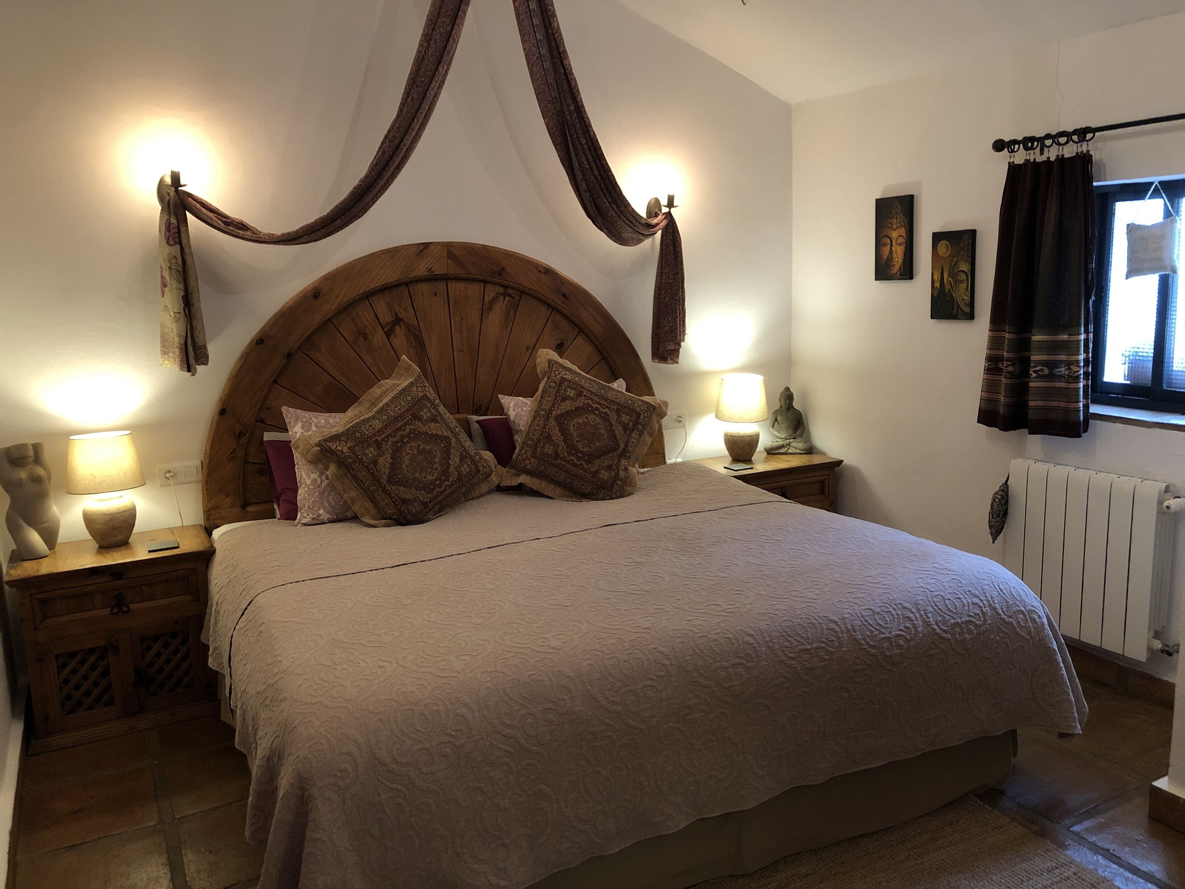 A bedroom with a large bed, wooden headboard, two bedside tables with lamps, and a window with curtains.