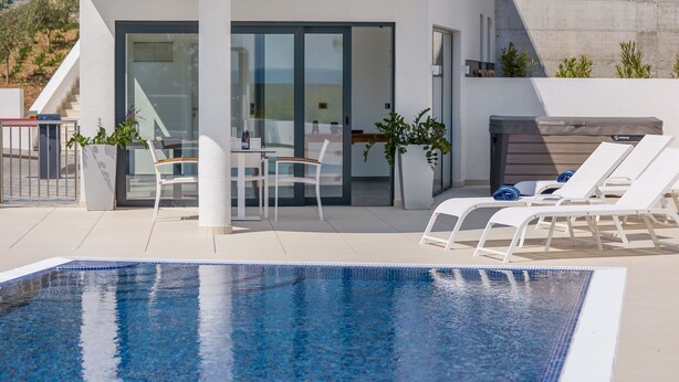 Ein moderner Poolbereich im Freien mit einer gläsernen Veranda, Liegestühlen und einem Tisch mit Stühlen.