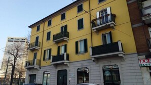 A multi-story yellow building with balconies, a visible storefront, and parked cars. - Tree House Along Canal Naviglio Grande (Milano)
