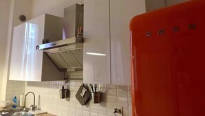 A kitchen with white cabinets, a stainless steel range hood, and a red appliance. - Tree House Along Canal Naviglio Grande (Milano)