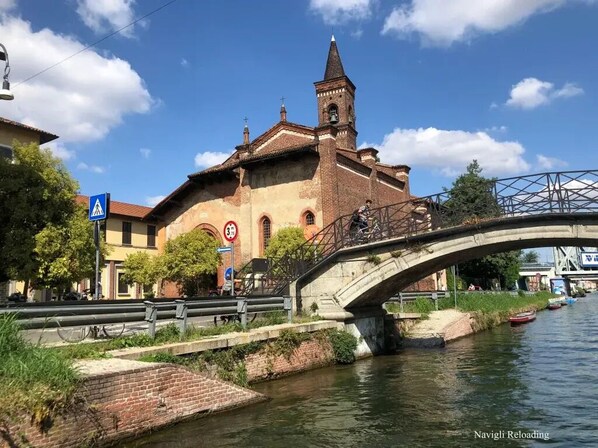 Une église historique dotée d’un clocher, un pont piétonnier et un canal où naviguent des bateaux.
