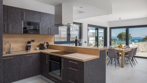 Une cuisine moderne avec des meubles de couleur sombre, un plan de travail en bois et un coin repas offrant une vue sur la mer.