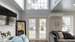 A modern living room with a grey sofa, a blue accent pillow, a coffee table, and a large window offering a view of the outside. - Blue Doors By The Sea by Bayley Vacation Rentals (Scarborough)
