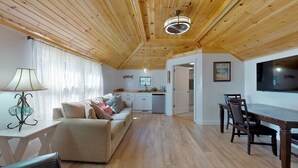 A cozy living room with a sofa, a dining table with chairs, a kitchen in the background, and a TV mounted on the wall. - Blue Doors By The Sea by Bayley Vacation Rentals (Scarborough)