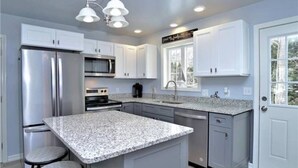 A modern kitchen with granite countertops, stainless steel appliances, and a large island with bar stools. - Blue Doors By The Sea by Bayley Vacation Rentals (Scarborough)