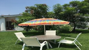 A round table with four white chairs and a colorful umbrella in a grassy outdoor area. - GREAT HOUSE LA MAGDALENA TEQUISQUIAPAN (Magdalena)