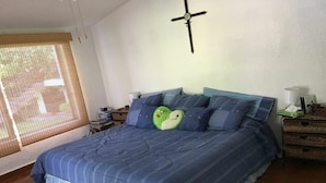 A bedroom with a large bed, a ceiling fan, a window with blinds, and a bedside table with a lamp and a green object on it. - GREAT HOUSE LA MAGDALENA TEQUISQUIAPAN (Magdalena)