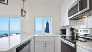 Eine moderne Küche mit weißen Schränken, einem Edelstahlbackofen und einem Fenster mit Meerblick.