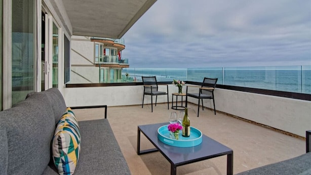 Ein Balkon mit einer Couch, Stühlen und einem Tisch mit Tablett und Blumen.