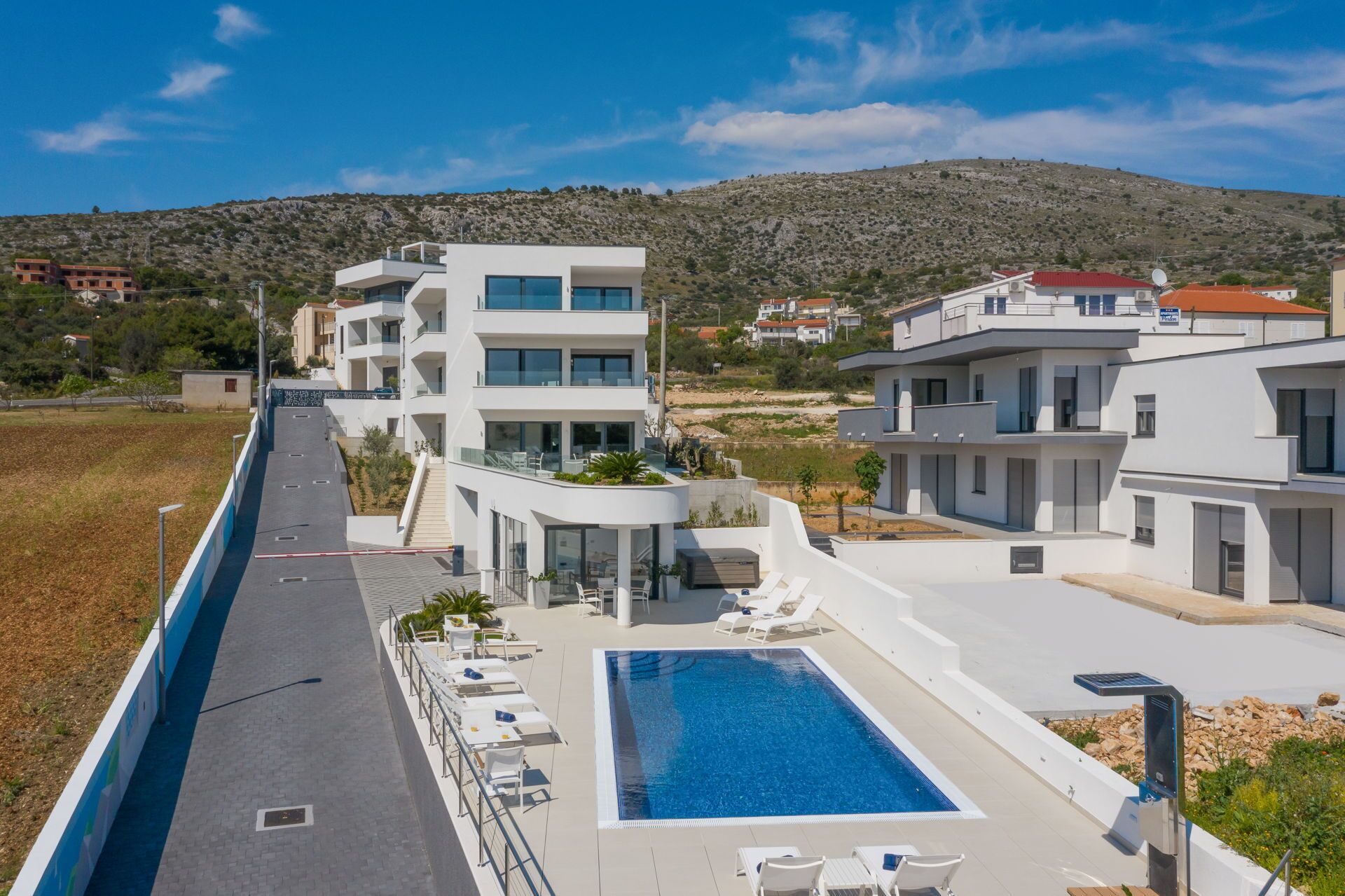 Un hotel moderno con piscina en la azotea, varios balcones y vistas a las colinas circundantes.