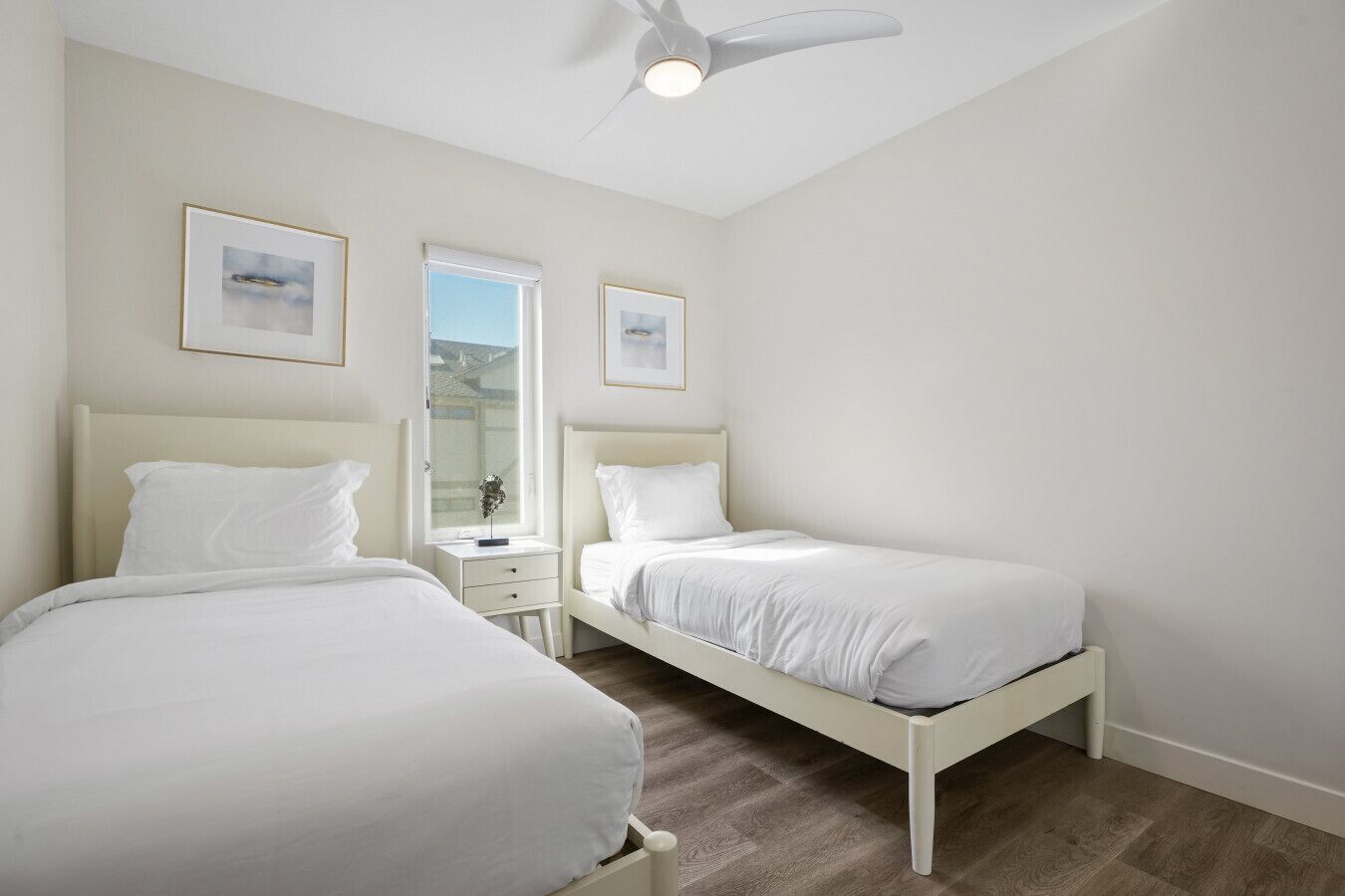 Une chambre avec deux lits, un ventilateur de plafond et des tableaux encadrés accrochés au mur.