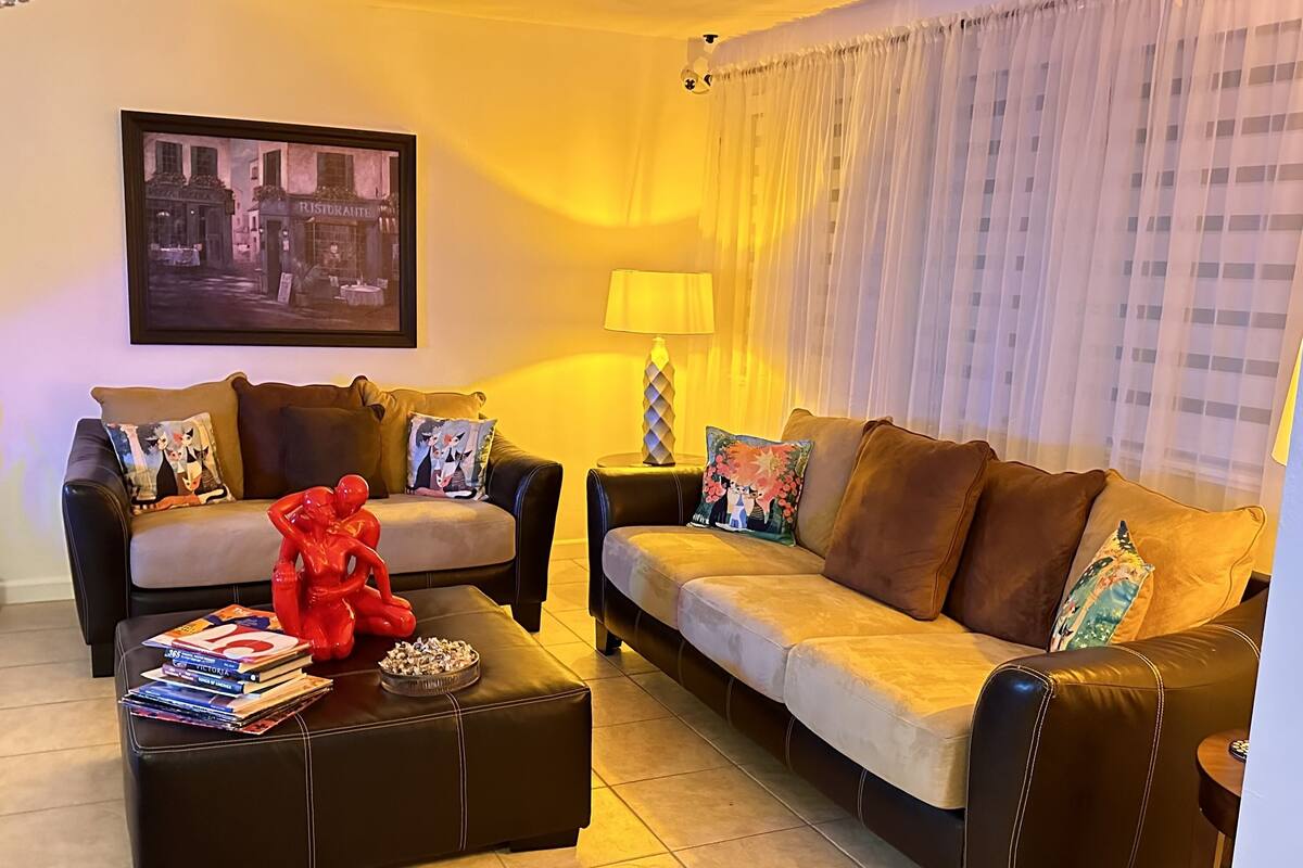 A living room with two sofas, a coffee table with books and a red sculpture, a framed picture on the wall, and a lamp.