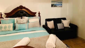 Une chambre avec un lit, un canapé noir et un tableau accroché au mur.