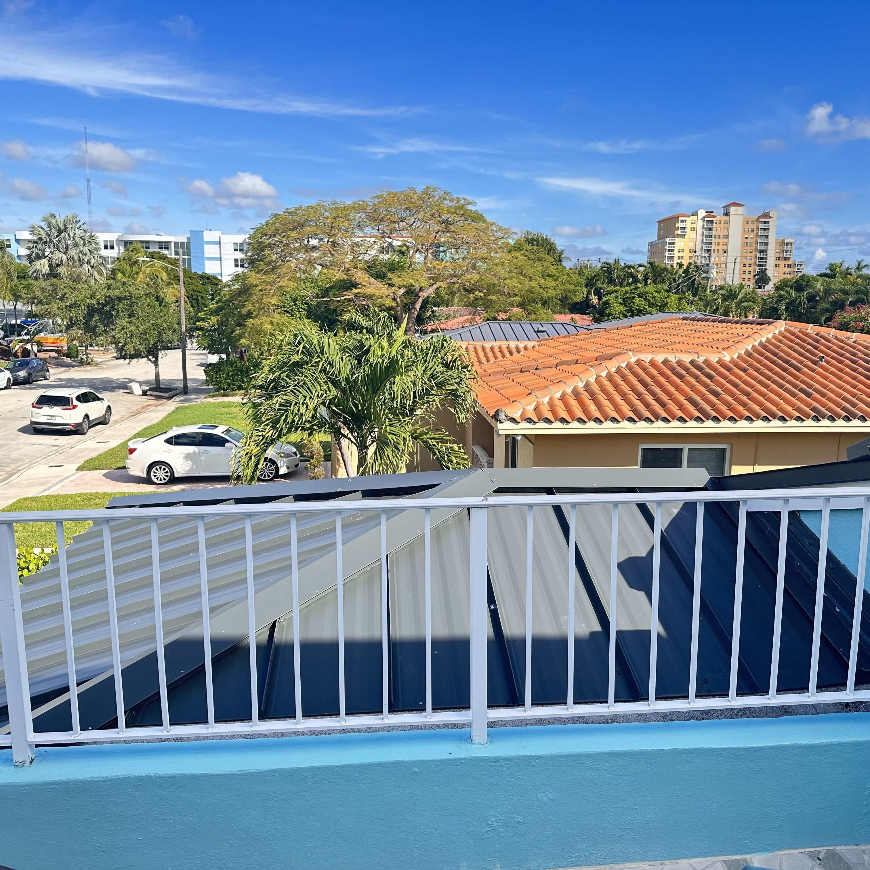 A residential area with a house featuring a tiled roof, a fenced yard, and parked cars.