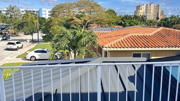 A residential area with a house featuring a tiled roof, a fenced yard, and parked cars.
