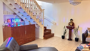Un salon avec un canapé en cuir noir, un meuble en bois, un escalier et une statue de Bouddha.