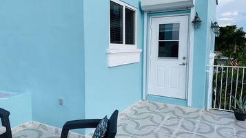 Um edifício azul com porta e janela brancas, um pátio ladrilhado e mobiliário de exterior.