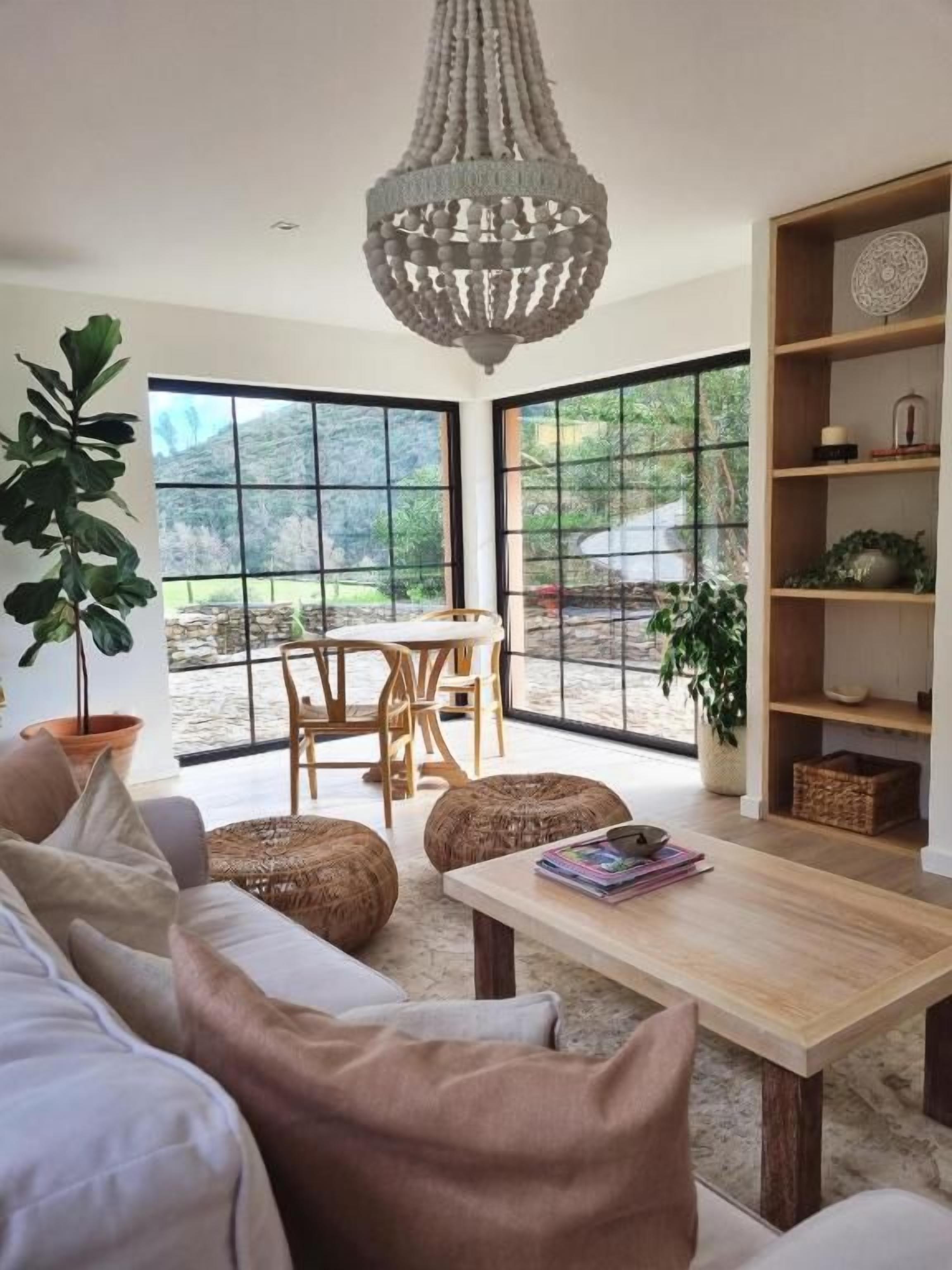 A modern living room with a sofa, coffee table, and a chandelier. There is a large window with a view of the outdoors.