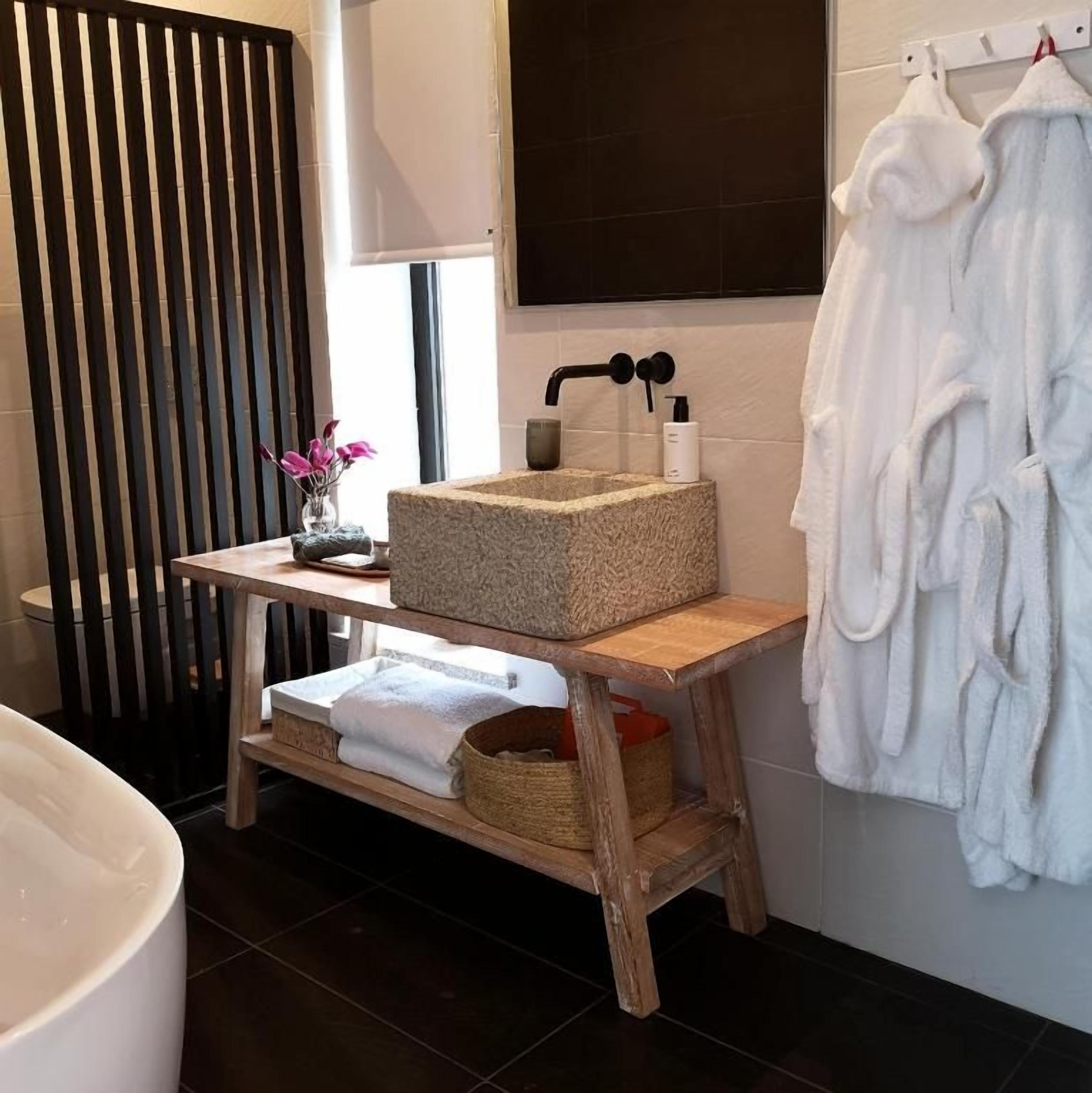 A bathroom with a wooden vanity, a large bathtub, and white towels.