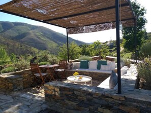 An outdoor patio with stone flooring, a round table with a vase of flowers, and a seating area with cushions and chairs. - Quinta das Levadas Country House & Nature (Oliveira do Hospital)