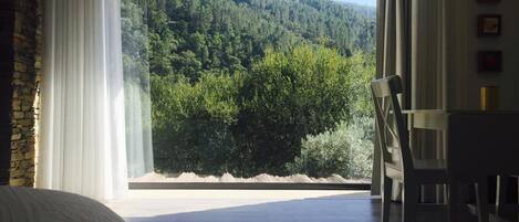 Un dormitorio con un ventanal que ofrece vistas a una ladera boscosa.