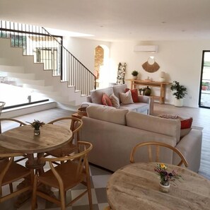Ein modernes Wohnzimmer mit Treppe, einer Sofagarnitur und einem Essbereich mit Holzmöbeln.