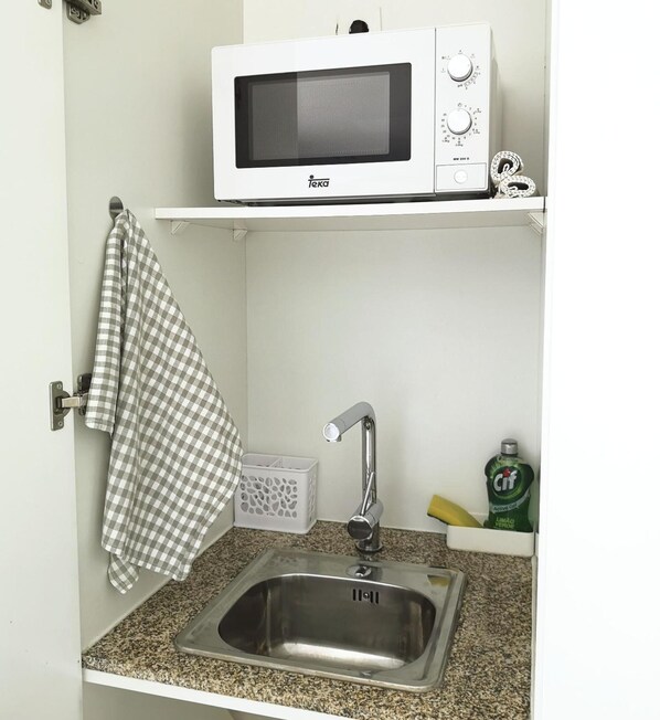A kitchen with a microwave on a shelf, a stainless steel sink, a checkered towel, a white basket, and a bottle of Cif. - Quinta das Levadas Country House & Nature (Oliveira do Hospital)