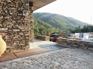 A stone patio with a wooden deck, stone walls, and a view of a forested hillside. - Quinta das Levadas Country House & Nature (Oliveira do Hospital)