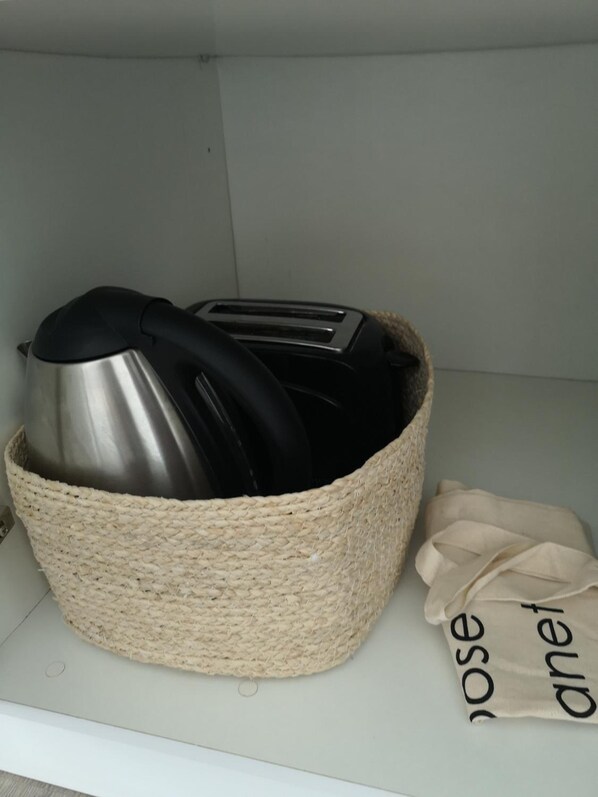 A woven basket containing a kettle, toaster, and black handles, placed on a shelf next to a beige cloth with the word "nose" partially visible. - Quinta das Levadas Country House & Nature (Oliveira do Hospital)