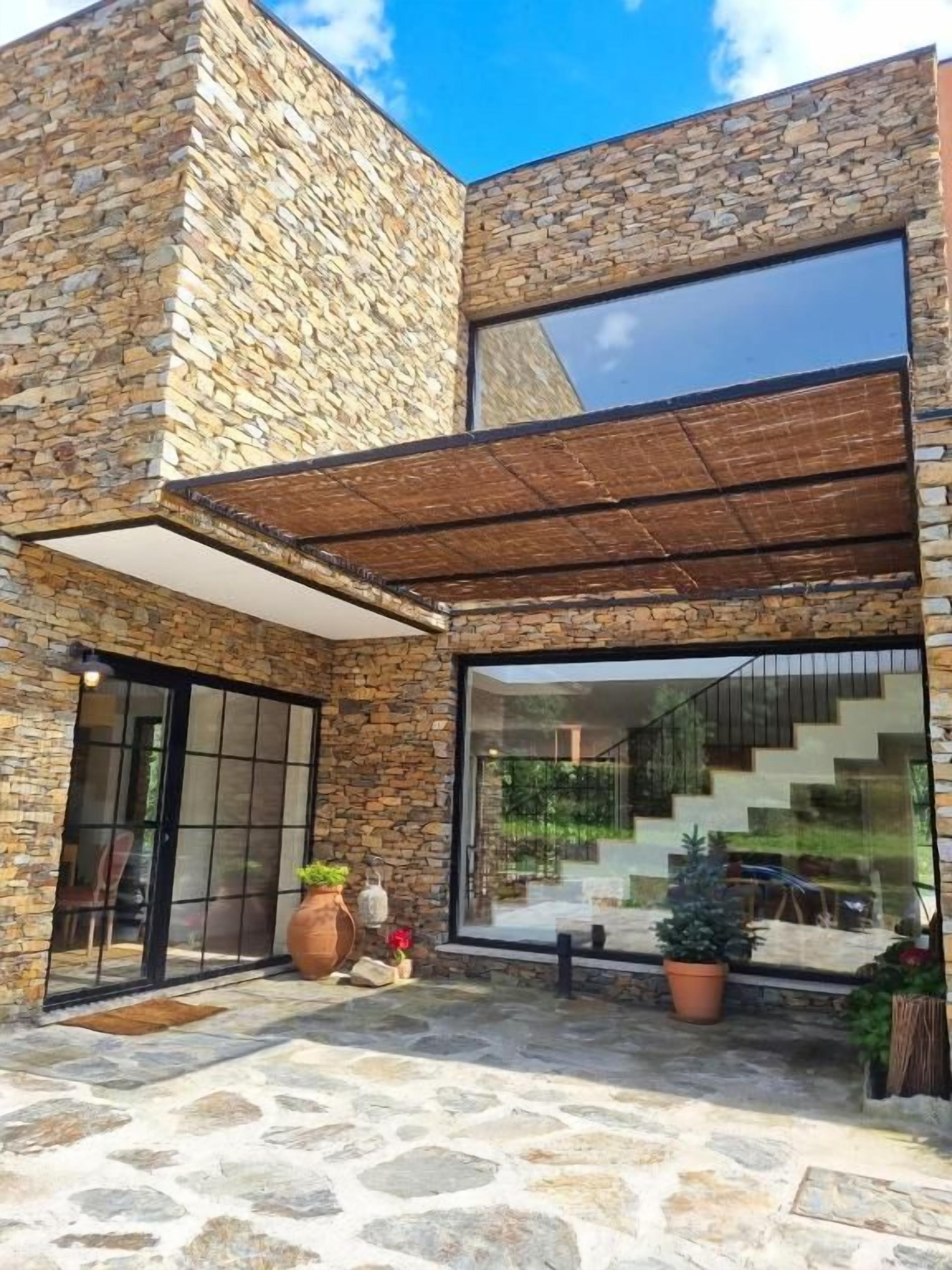 Un edificio moderno con fachada de piedra, grandes ventanales y un área exterior cubierta con plantas en macetas.