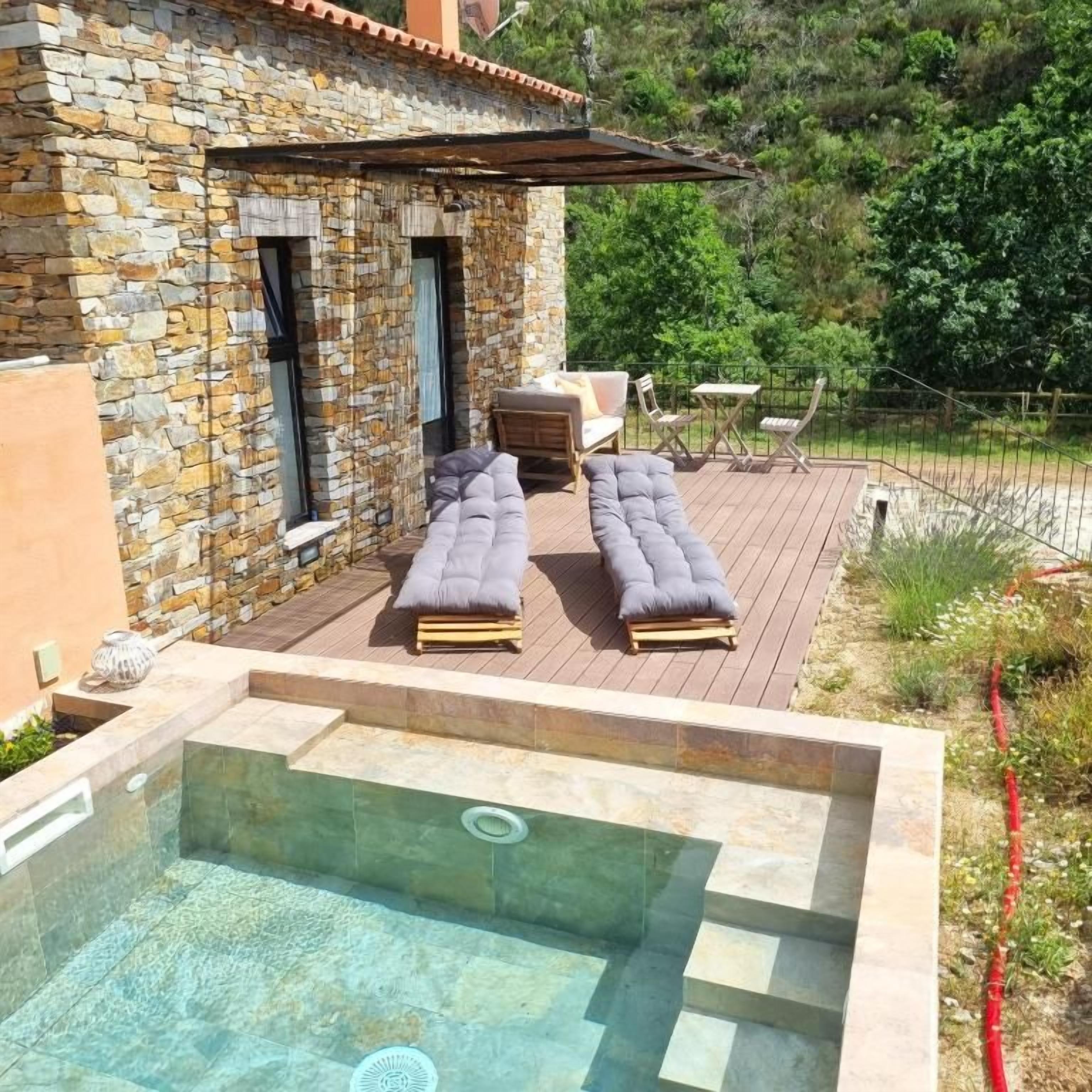 A stone building with a pool area, outdoor seating, and a view of greenery.
