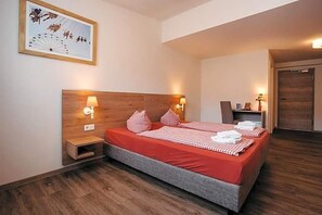 A double bed with red bedding, two bedside lamps, a wooden headboard, a small bedside table, and a framed picture on the wall.