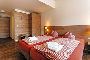 A hotel room with two beds, wooden headboard, and a bench.