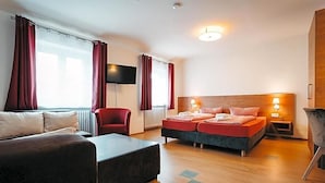 A modern hotel room with a sofa, a bed, a TV, and a window with curtains.