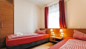 A hotel room with two beds, a wooden wardrobe, a window with curtains, and bedside lamps.