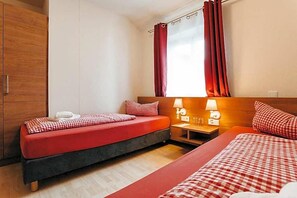 A hotel room with two beds, a wooden wardrobe, a window with curtains, and bedside lamps.
