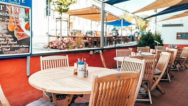An outdoor seating area with wooden tables and chairs, a menu board, and a view of the street.