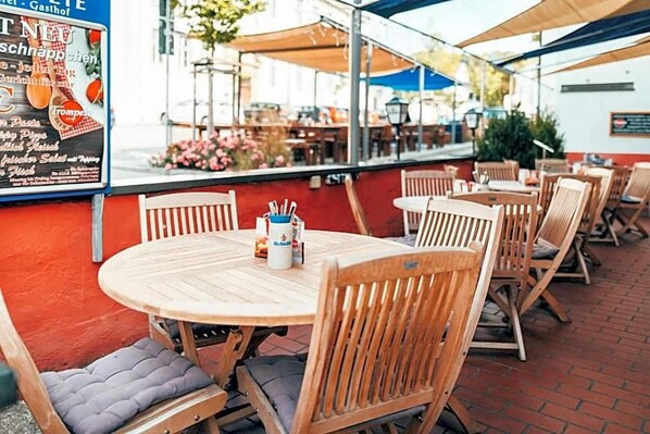 An outdoor seating area with wooden tables and chairs, a menu board, and a view of the street.