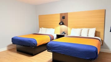 A hotel room with two beds, wooden headboard, bedside tables, and a nightstand with a lamp.