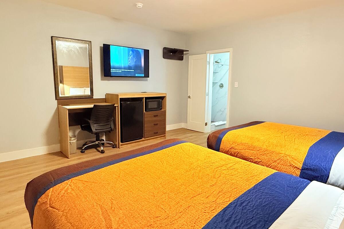 Un dormitorio con dos camas, un escritorio, un televisor y una puerta que da a un baño.