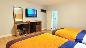 A bedroom with two beds, a desk, a television, and a door leading to a bathroom.