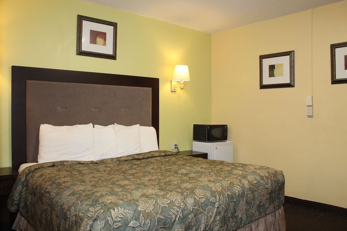 Habitación de hotel con una cama grande, una mesita de noche, una lámpara de pared y un microondas.